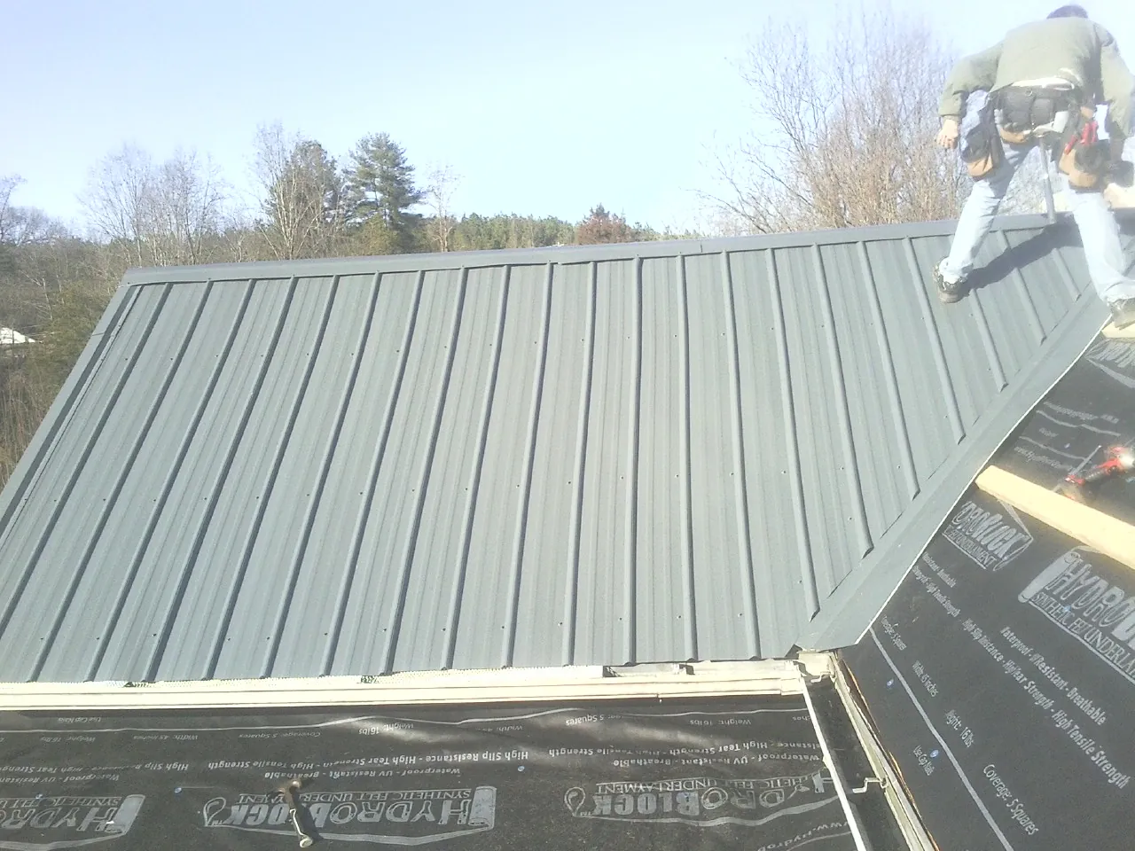 Crew installing dark green standing seam panels over synthetic underlayment in Arizona City