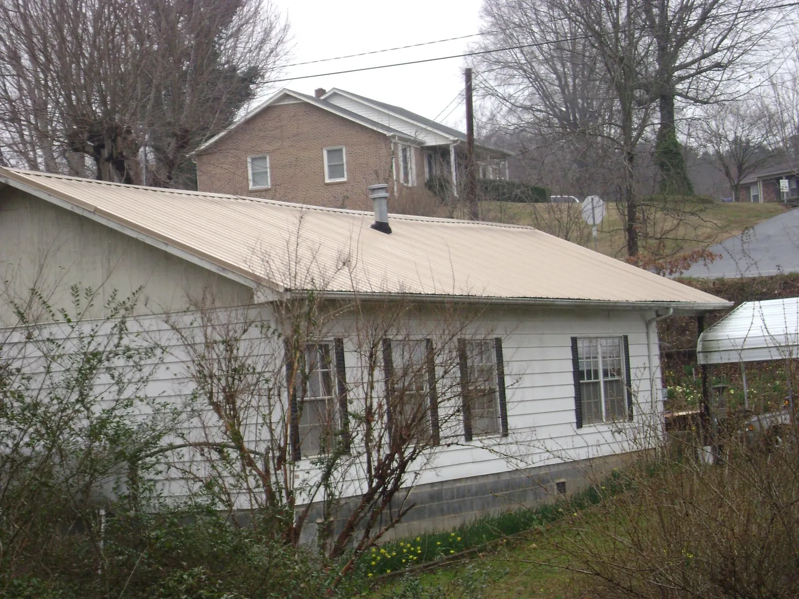 Tan metal roof on a white sided house set into a hillside — Commercial Roofing by Roofing Brothers in Arizona City
